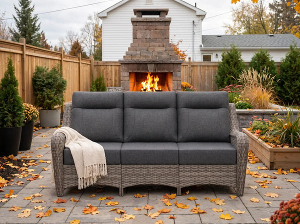 OuterCraft 3-seater wicker sofa with dark gray cushions styled on a luxury autumn patio with stone fireplace.