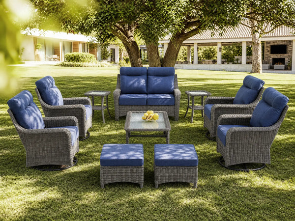 OuterCraft 10-piece dark PE rattan patio set with loveseat, 360-degree swivel rocker chairs, ottomans, side table and coffee table set with 6-inch thick blue cushions styled on a grand estate patio