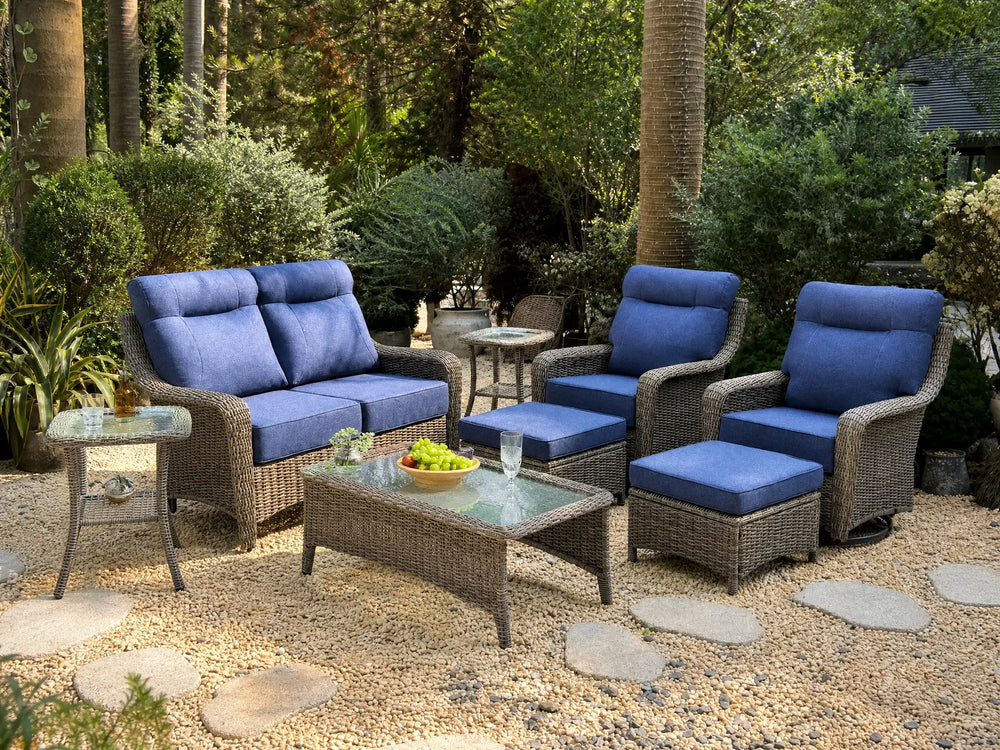 OuterCraft 8-piece dark PE rattan patio set with loveseat, 360-degree swivel rocker chairs, ottomans, coffee table and side table set with 6-inch thick blue cushions styled on a grand estate patio