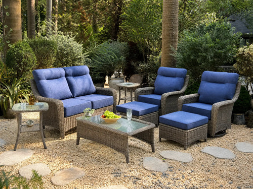 OuterCraft 8-piece dark PE rattan patio set with loveseat, 360-degree swivel rocker chairs, ottomans, coffee table and side table set with 6-inch thick blue cushions styled on a grand estate patio