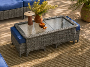 OuterCraft dark PE wicker coffee table with glass top and two nested ottomans with blue cushions styled on patio