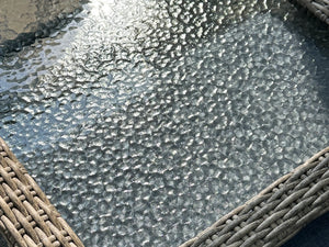 Macro close-up of OuterCraft dark wicker patio table featuring water-ripple tempered glass top and hand-woven heavy-duty PE wicker trim