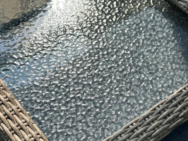Macro close-up of OuterCraft dark wicker patio table featuring water-ripple tempered glass top and hand-woven heavy-duty PE wicker trim