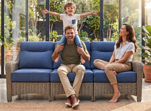 OuterCraft 3-seater wicker sofa with blue cushions showcased in a warm family lifestyle patio setting.