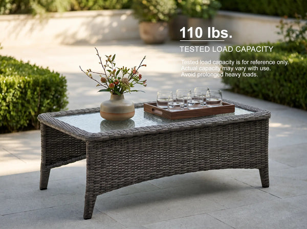 OuterCraft all-weather patio wicker coffee table with a tempered glass top, supporting a wooden serving tray and decor to highlight a tested 110 lbs load capacity and reinforced frame durability.