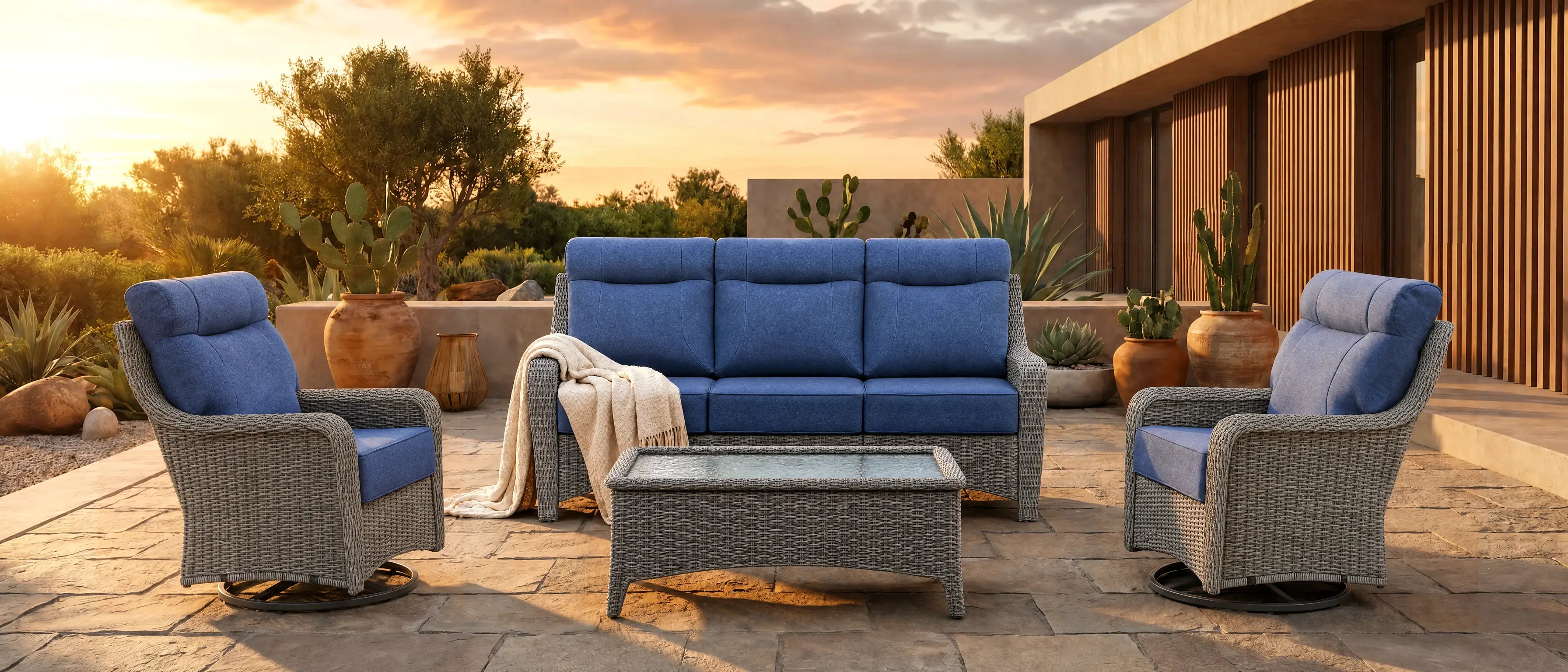 OuterCraft outdoor dark wicker furniture set featuring 3-seater sofa, 2 swivel rocker chairs, and coffee table in blue Olefin cushions on villa courtyard patio at sunset