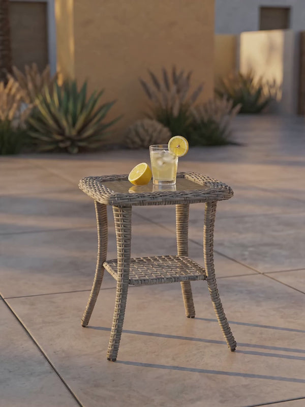 OuterCraft 2-tier all-weather wicker patio side table with tempered glass top holding iced beverage in golden hour sunlight