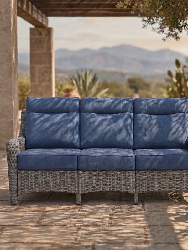 OuterCraft 3-seater patio sofa close-up showing blue solution-dyed Olefin cushion texture, high-back ergonomic seams, and hand-woven PE wicker base under natural sunlight shadows
